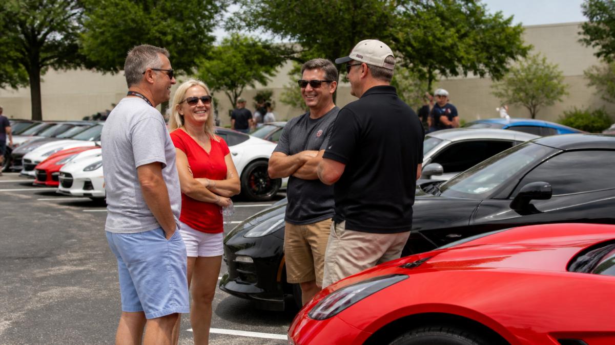 Corvette owners chatting and smiling at an outdoor car club meeting to join a car club